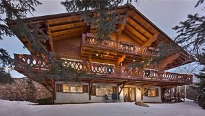 Un chalet en bois doté d’un balcon, d’un mur en pierre et entouré d’un paysage enneigé.