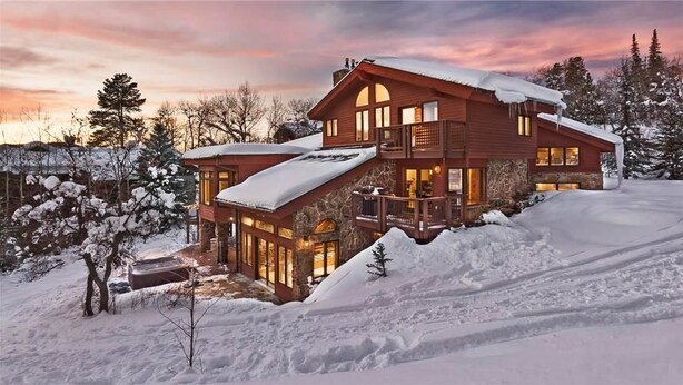 A large, multi-story wooden house with a snow-covered roof and a stone foundation, surrounded by snow-covered trees and a clear sky. - Trails Edge Lodge (Steamboat Springs)