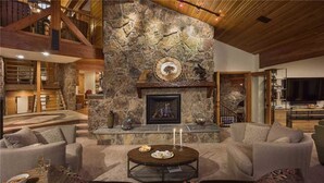 A spacious living room with a stone fireplace, comfortable seating, and a high ceiling with exposed beams. - Trails Edge Lodge (Steamboat Springs)