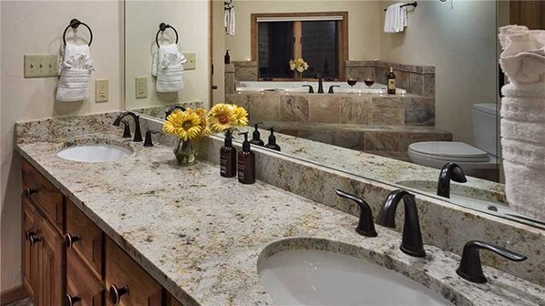 A bathroom with a granite countertop, two sinks, a large mirror, and a towel rack.