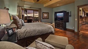 A bedroom with a large bed, a TV, a wooden dresser, and a view of the outdoors.