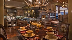 A spacious dining area with a large wooden table set for a meal, surrounded by wooden chairs.