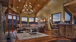 A spacious living room with a large sectional sofa, a wooden bar area, and large windows offering a mountain view.