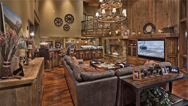 A spacious living area with a large sofa, a coffee table, and a fireplace. There is a bar area with stools and a television mounted on the wall.