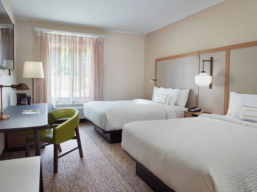 Habitación de hotel con dos camas, un escritorio, una silla, una lámpara y una ventana con cortinas.