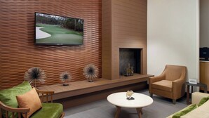 A modern living room with a television mounted on a wooden wall, a fireplace, and a seating area with a green sofa and a beige armchair. - Fairfield Inn & Suites by Marriott Asheville Airport/Fletcher (Fletcher)