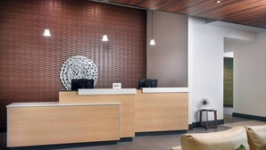 A modern reception area with wooden paneling, a reception desk, two pendant lights, and a leather sofa with a green pillow. - Fairfield Inn & Suites by Marriott Asheville Airport/Fletcher (Fletcher)