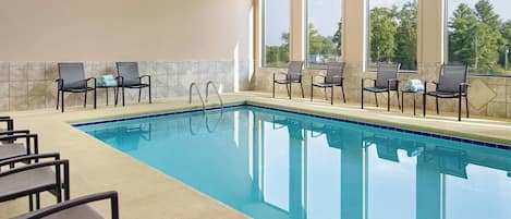 A swimming pool with chairs and a view of trees through large windows.