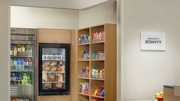 A kitchenette with a refrigerator, a freezer, and shelves stocked with snacks and beverages.