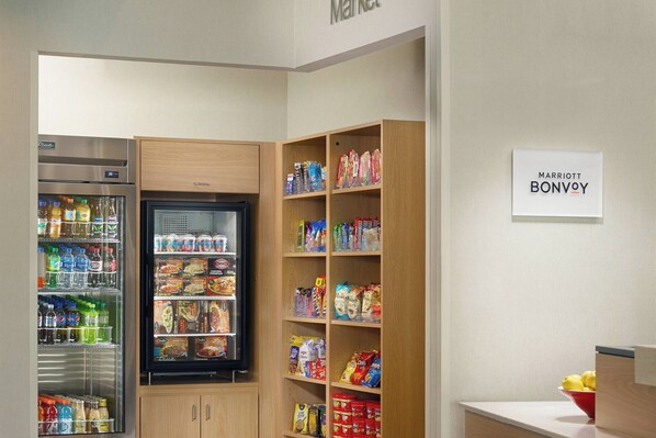 A kitchenette with a refrigerator, a freezer, and shelves stocked with snacks and beverages.
