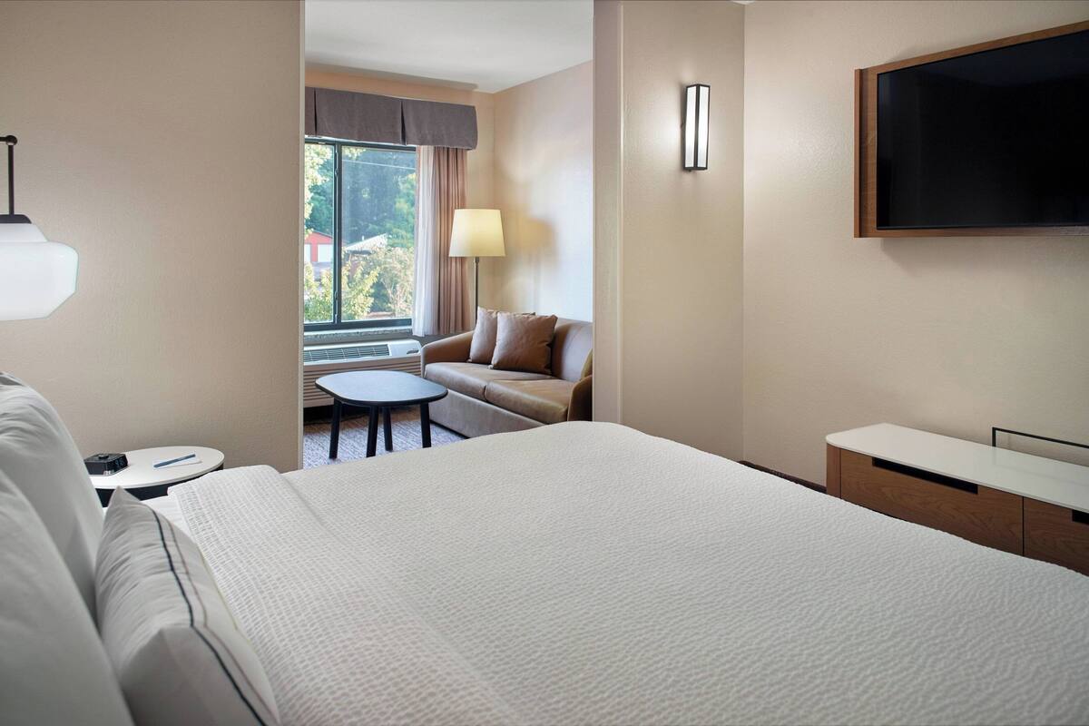 Une chambre d’hôtel avec un grand lit, une petite table ronde, un canapé et un téléviseur fixé au mur.