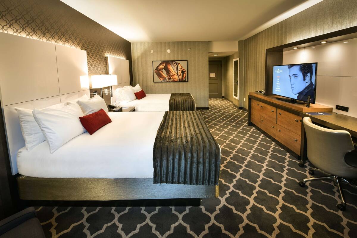 Une chambre d’hôtel avec un grand lit, un bureau, une télévision et une moquette à motifs.