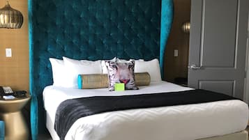 Una habitación de hotel moderna con una cama grande, un cabecero de madera, una mesita de noche con lámpara y una puerta.