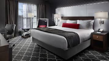 Una habitación de hotel con una cama grande, dos mesitas de noche con lámparas, una silla, un escritorio y una alfombra estampada.