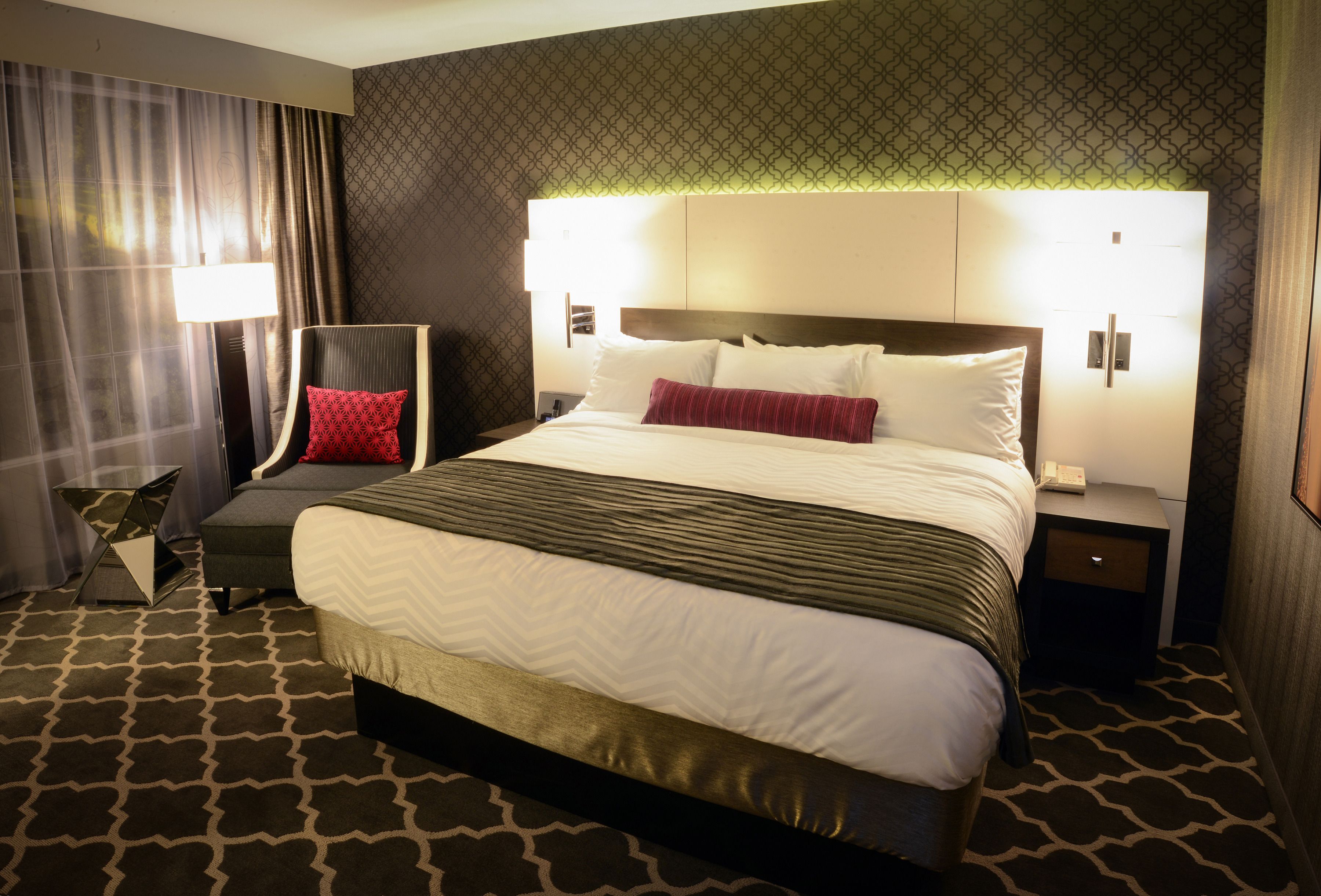 Ein Hotelzimmer mit einem großen Bett, einem Nachttisch, einer Lampe und einem gemusterten Teppich.