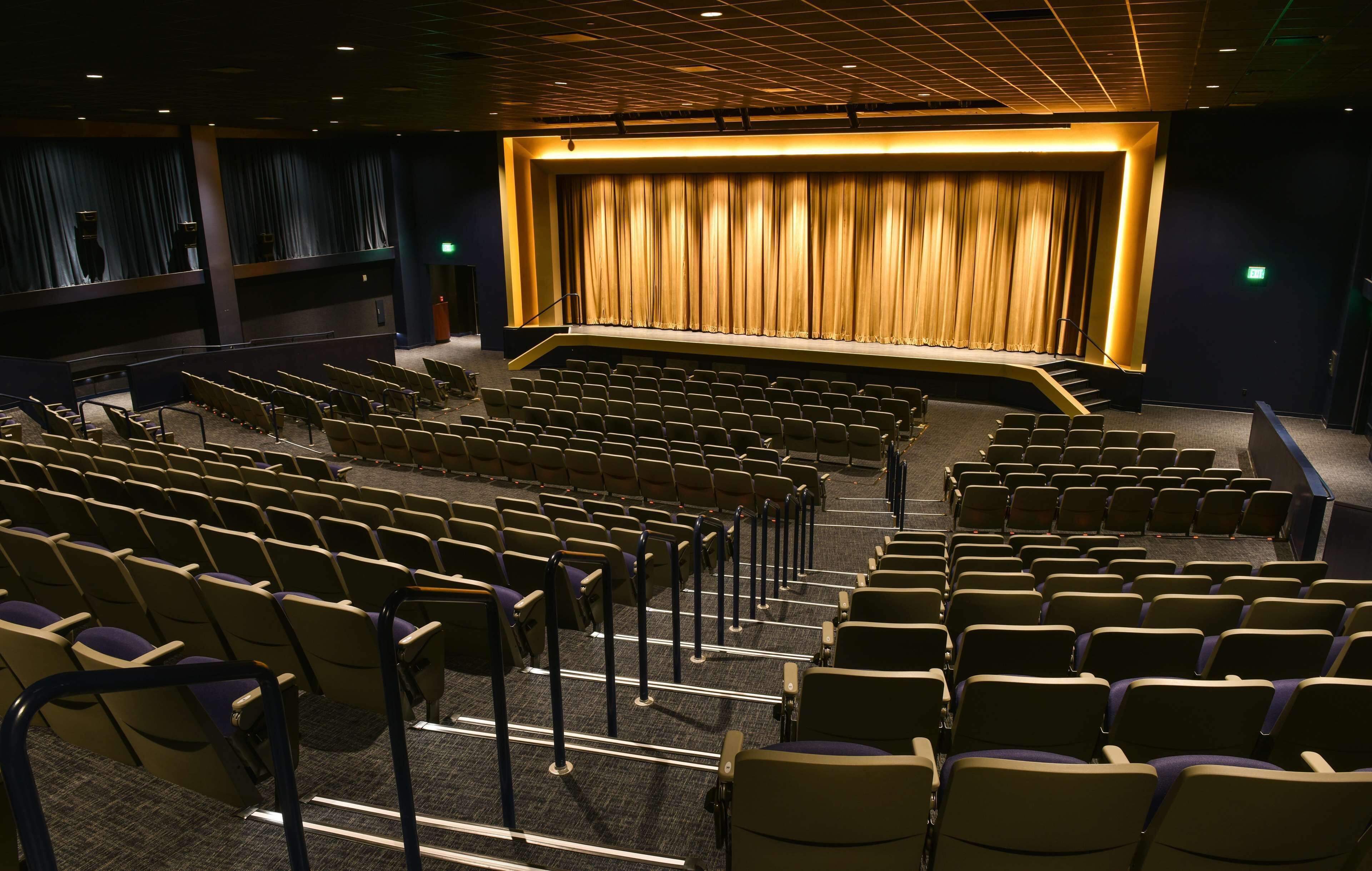 Un teatro con hileras de asientos y un escenario con cortinas.