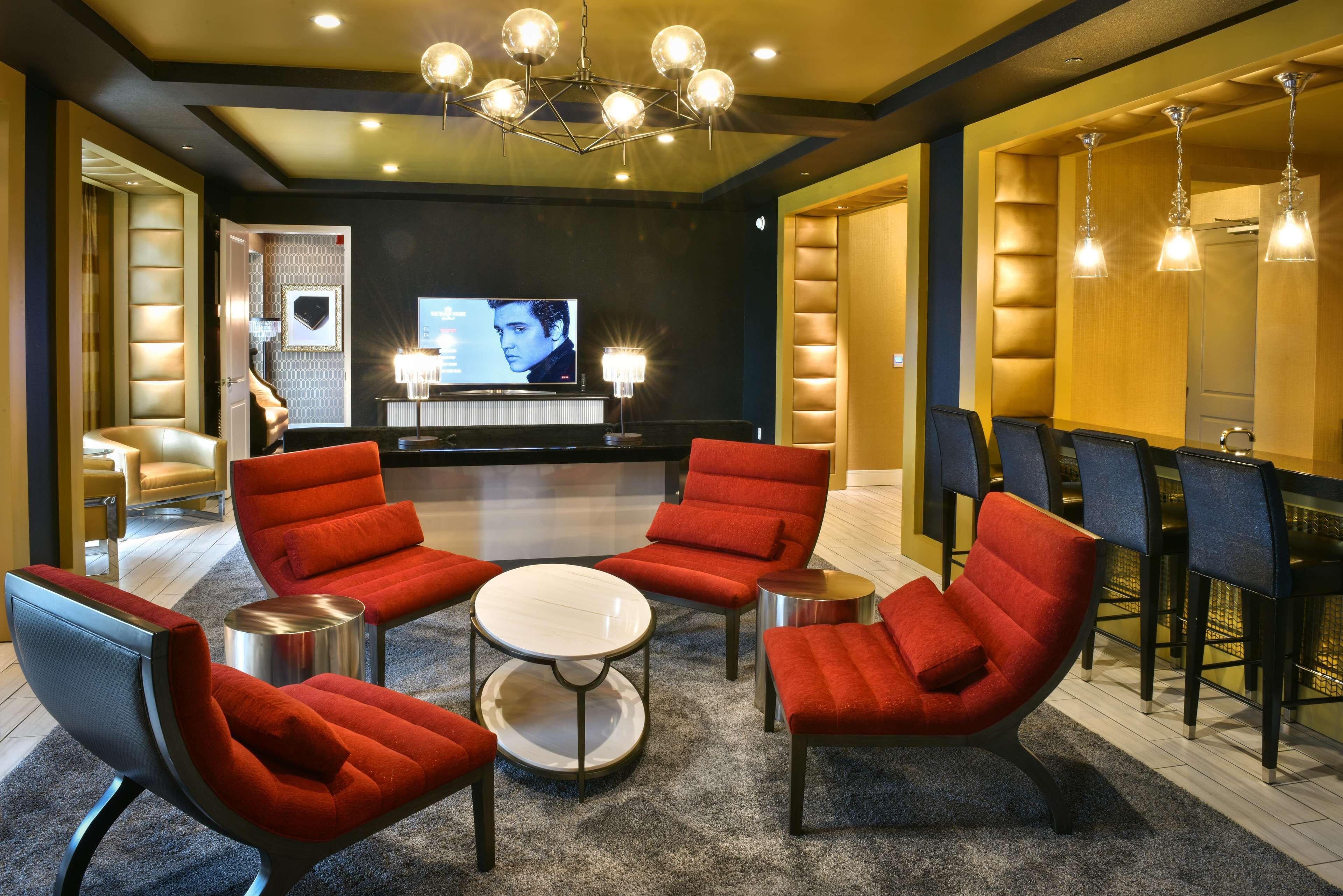 A modern lounge area with red upholstered chairs, a round table, and a television screen.
