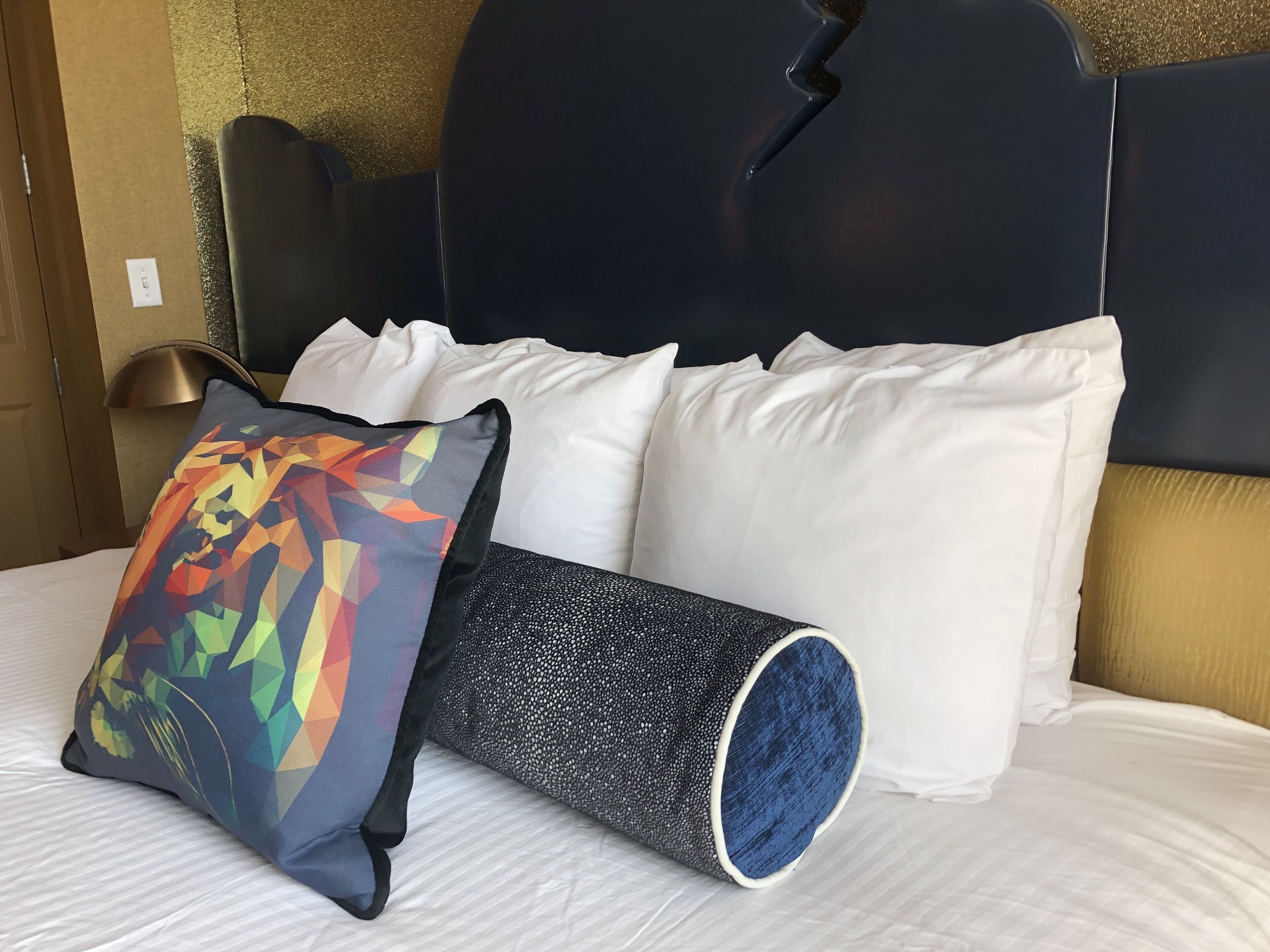 A bed with white pillows, a colorful geometric pillow, and a cylindrical black and white pillow.