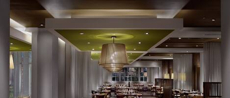 A spacious dining area with multiple tables and chairs, a large hanging light fixture, and a green accent wall.