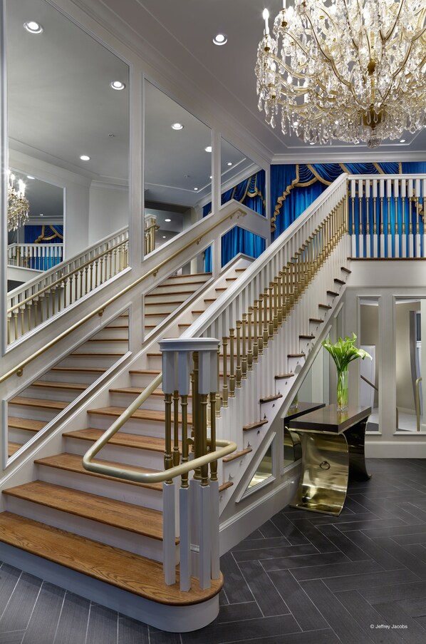 A grand staircase with a golden handrail, a chandelier, and a blue curtain backdrop.