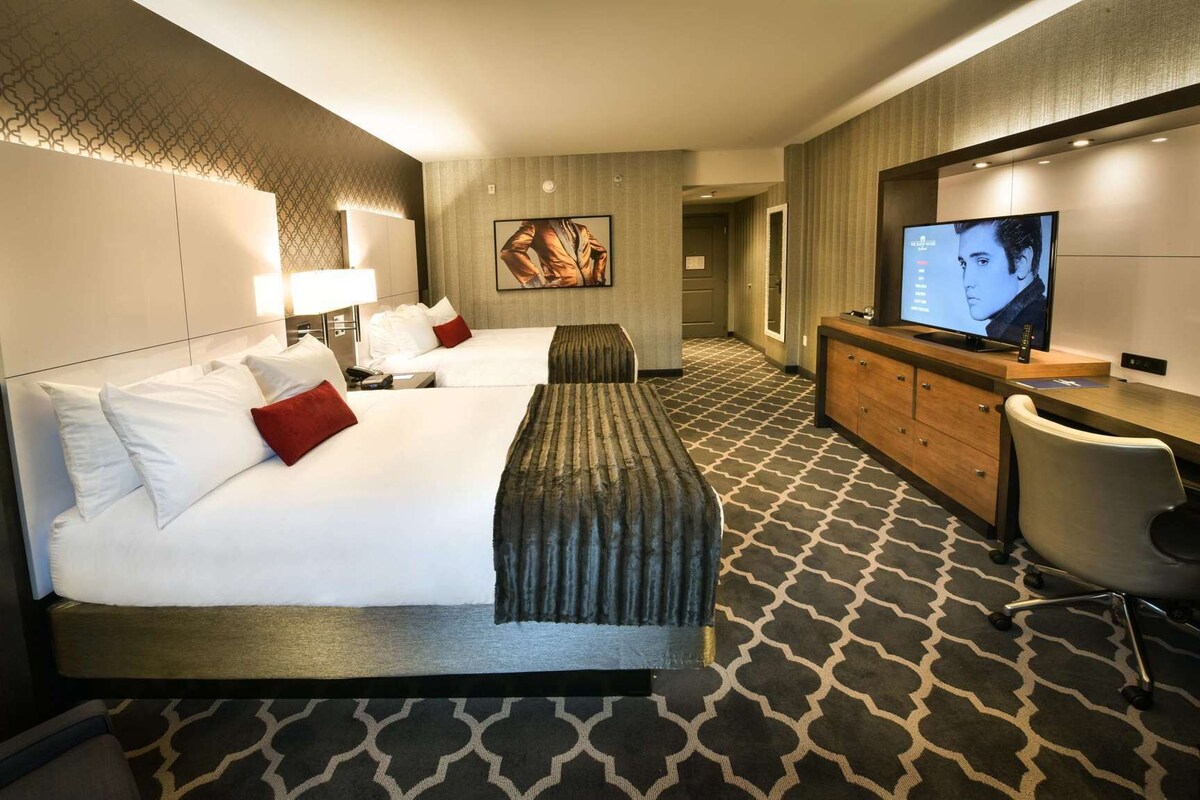 A hotel room with a large bed, a TV, a desk with a computer, and a seating area.