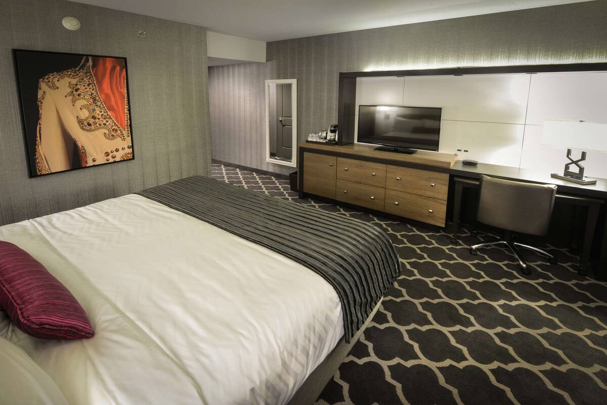 Une chambre d’hôtel avec un grand lit, une télévision, un bureau et une salle de bain à l’arrière-plan.