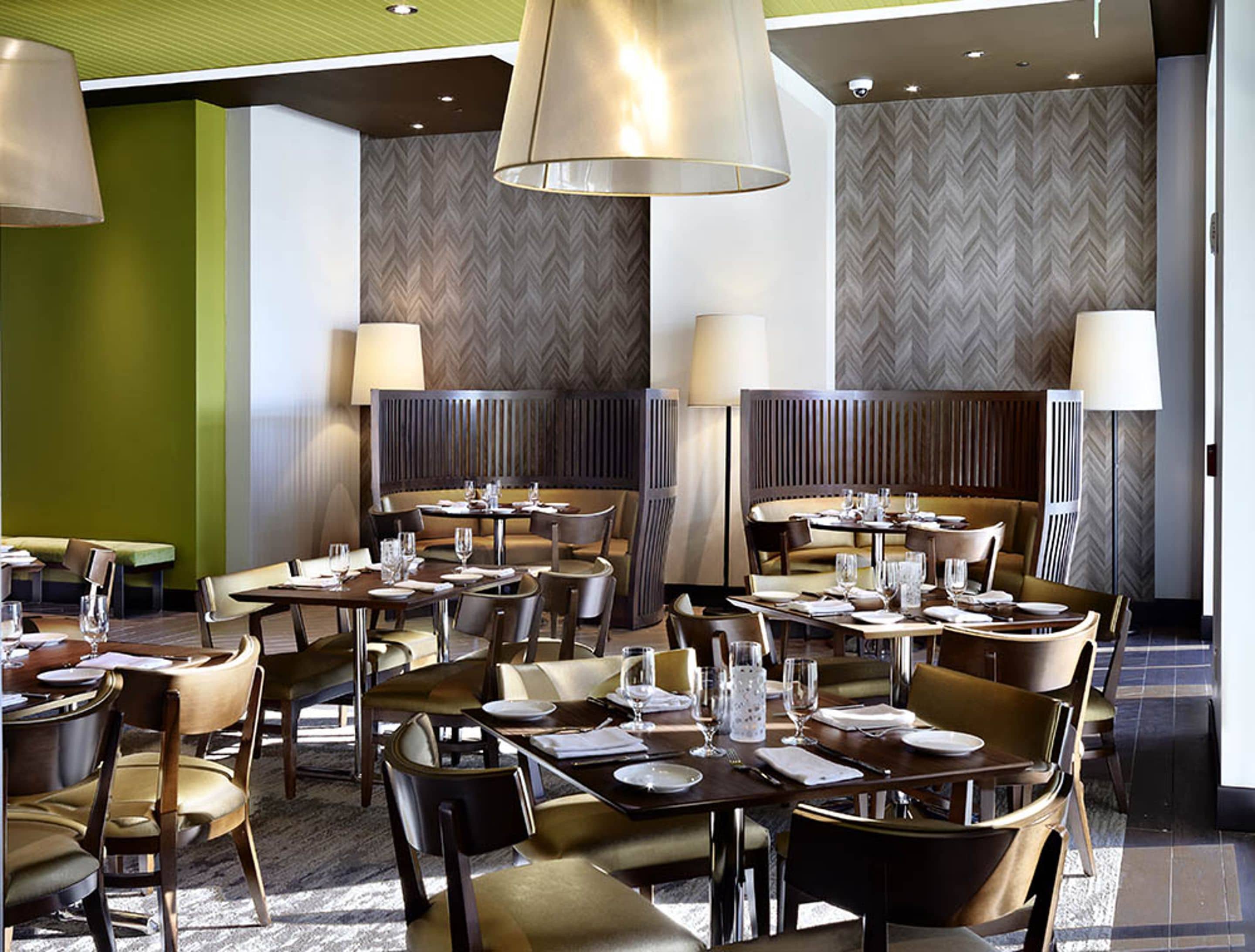 A modern restaurant with multiple dining tables and chairs, ambient lighting, and a herringbone-patterned wall.