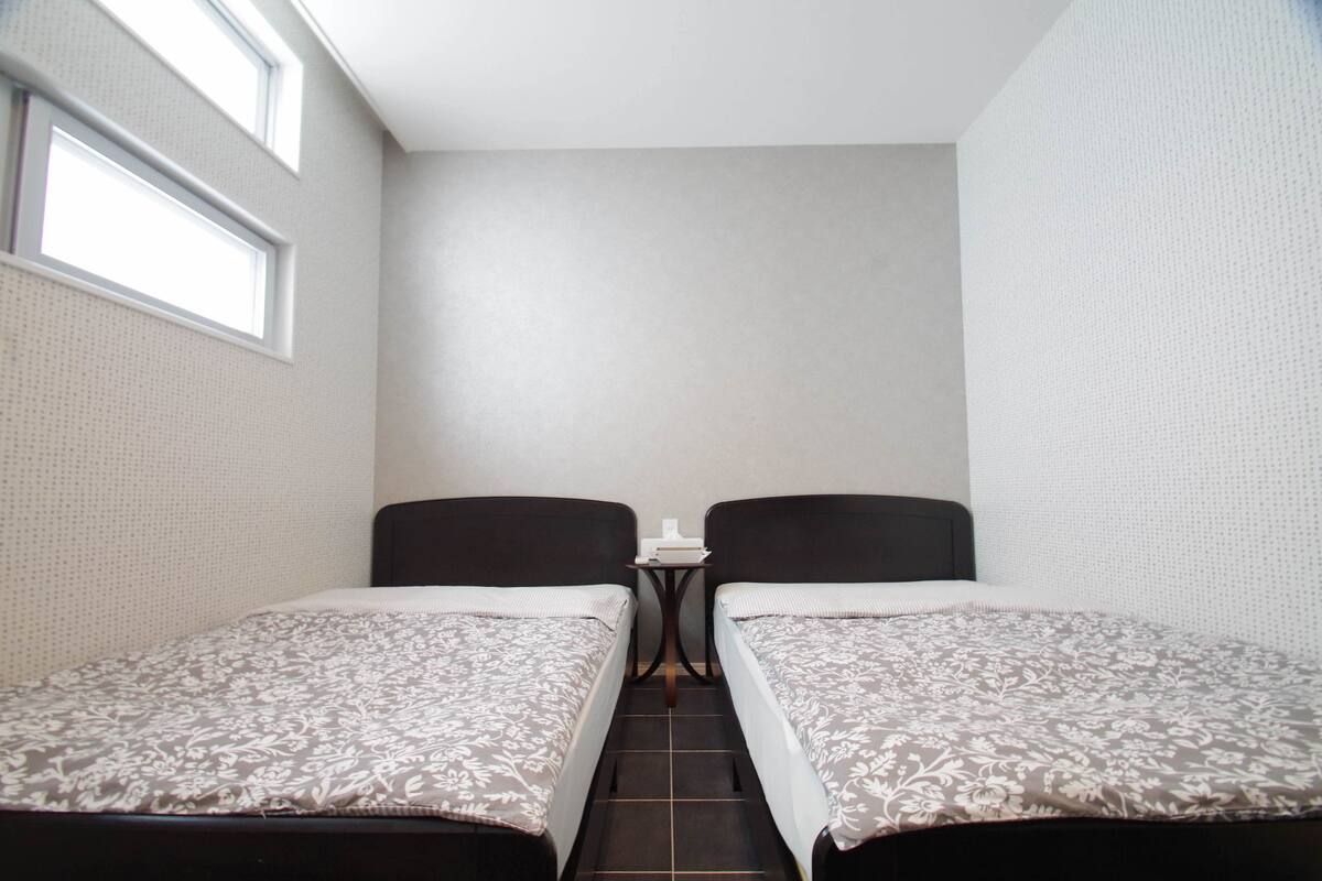 A small, narrow room with two single beds, a small table, and a window.
