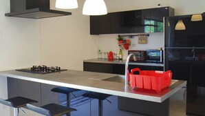 A modern kitchen with a central island, black cabinets, stainless steel appliances, and pendant lighting.