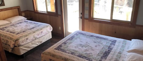 A room with two beds, wooden paneling, and windows with curtains.