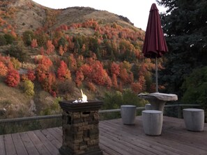 A stone fire pit with a red umbrella on a wooden deck, surrounded by concrete planters, overlooking a hillside with autumn foliage. - Lava Hot Springs East KOA Holiday (Lava Hot Springs)