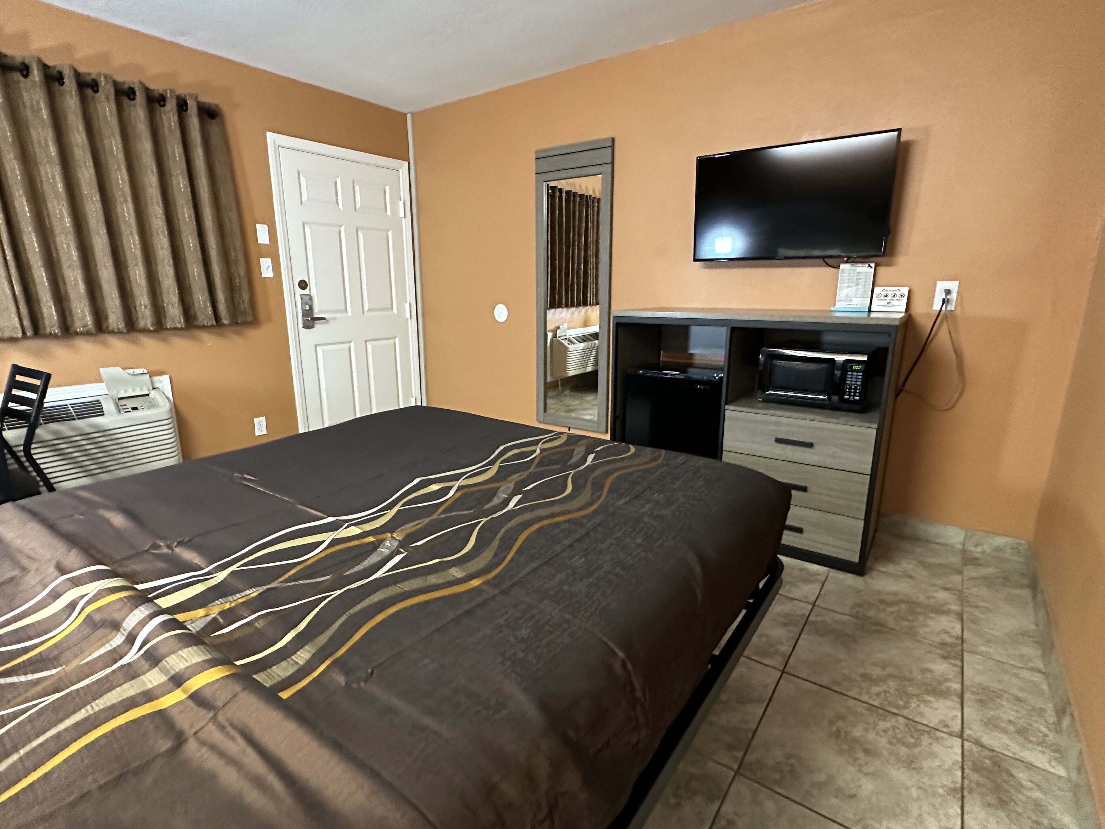 A hotel room with a bed, a desk with a microwave, a TV, and a door.