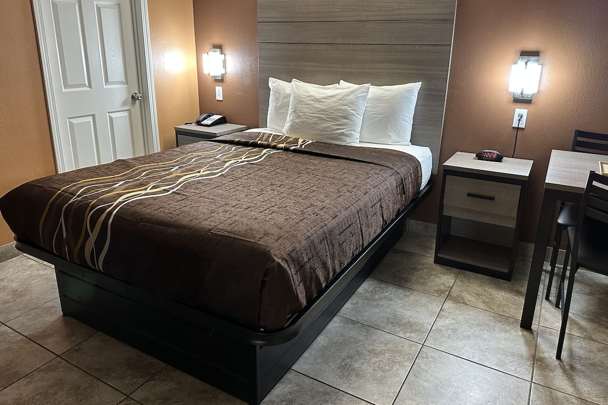 A hotel room with a bed, bedside tables, a desk, and a chair.