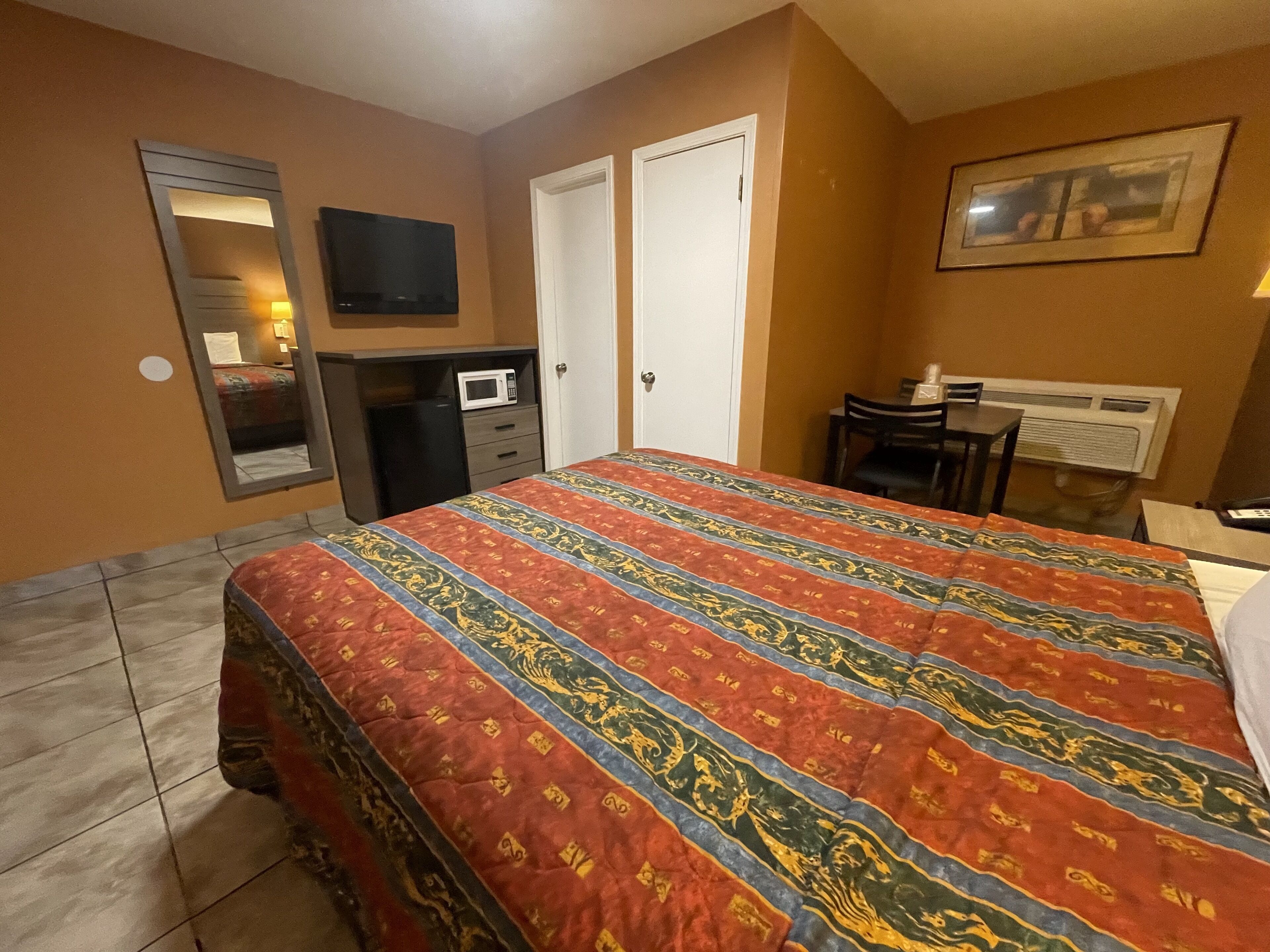 Habitación de hotel con cama, escritorio, silla, televisor, microondas y puerta.