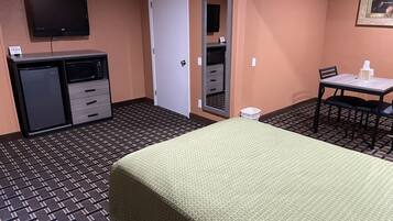 Ein Hotelzimmer mit Bett, Schreibtisch, Stuhl, Fernseher, Minikühlschrank und Kleiderschrank.