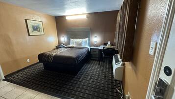A hotel room with a bed, bedside tables, a desk, and a heater.