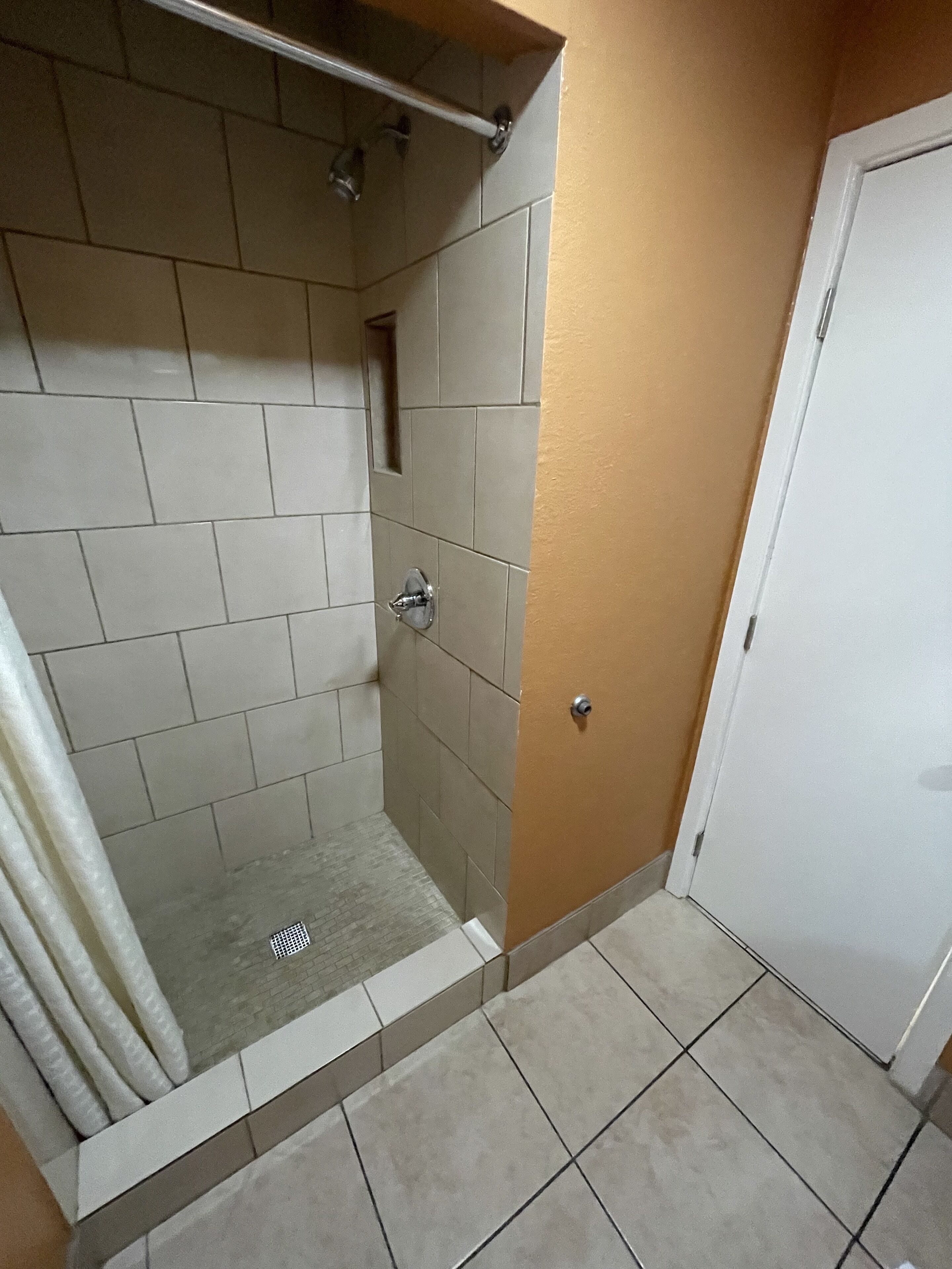 A shower area with tiled walls and floor, a showerhead, and a door.