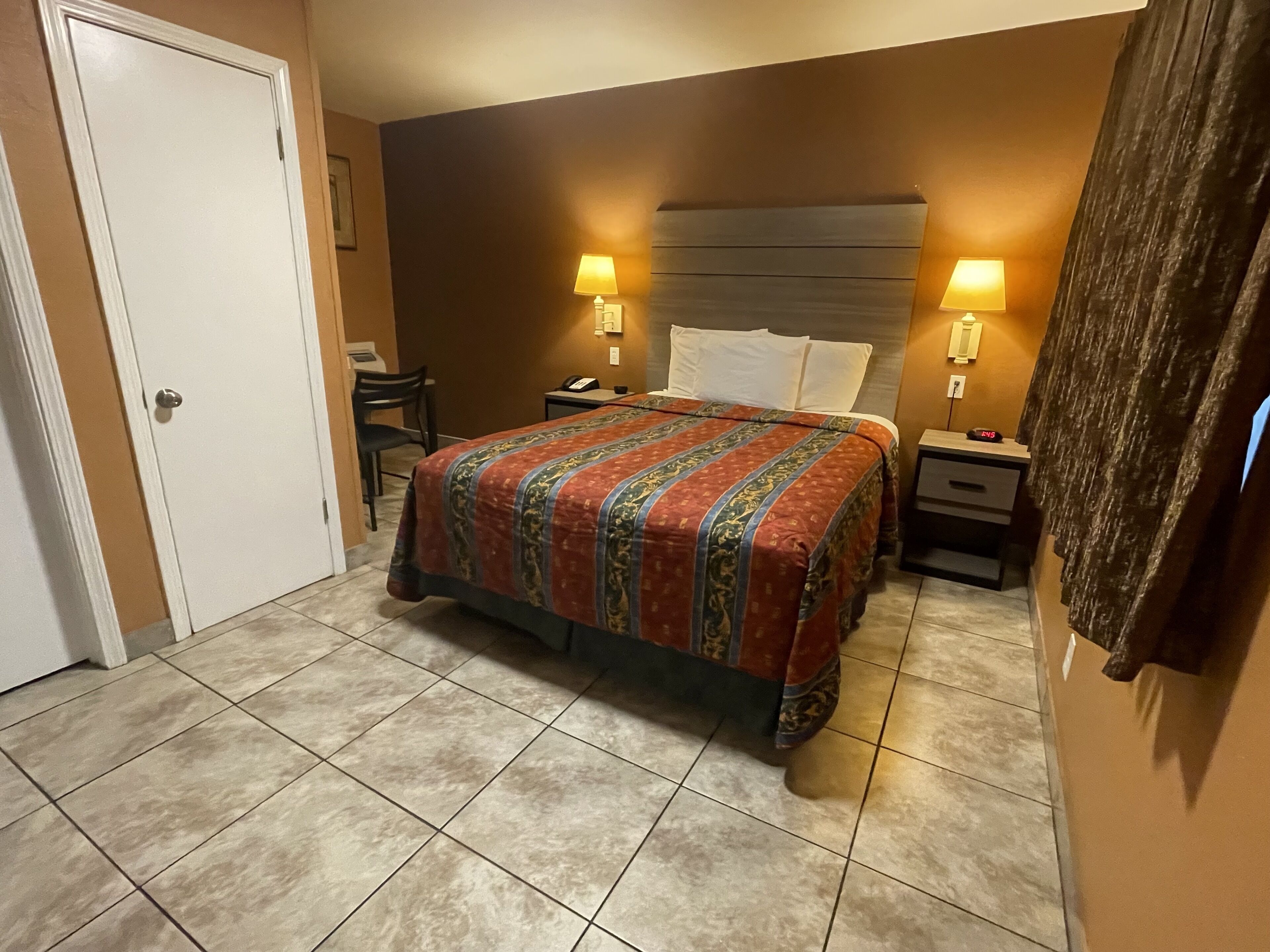 Una habitación de hotel con una cama grande, dos mesitas de noche con lámparas, un escritorio con silla y una puerta.