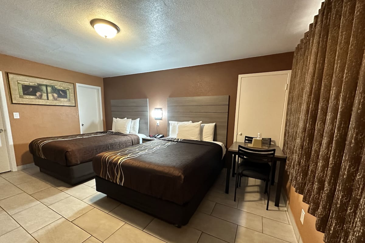 A hotel room with two beds, a desk, and a chair.