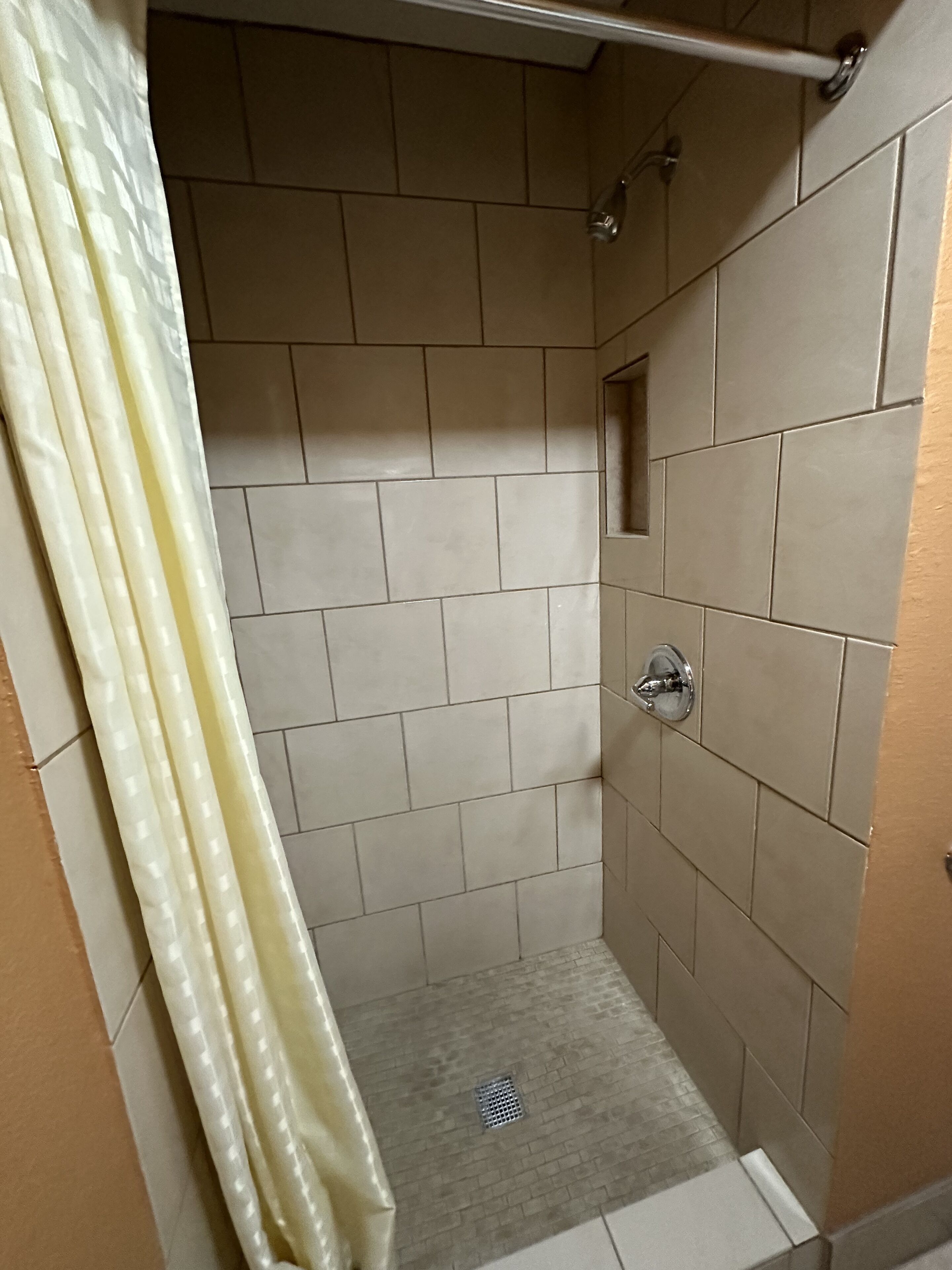 Un pequeño box de ducha con azulejos, cabezal de ducha y desagüe.