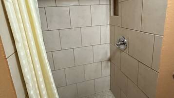 Un pequeño box de ducha con azulejos, cabezal de ducha y desagüe.