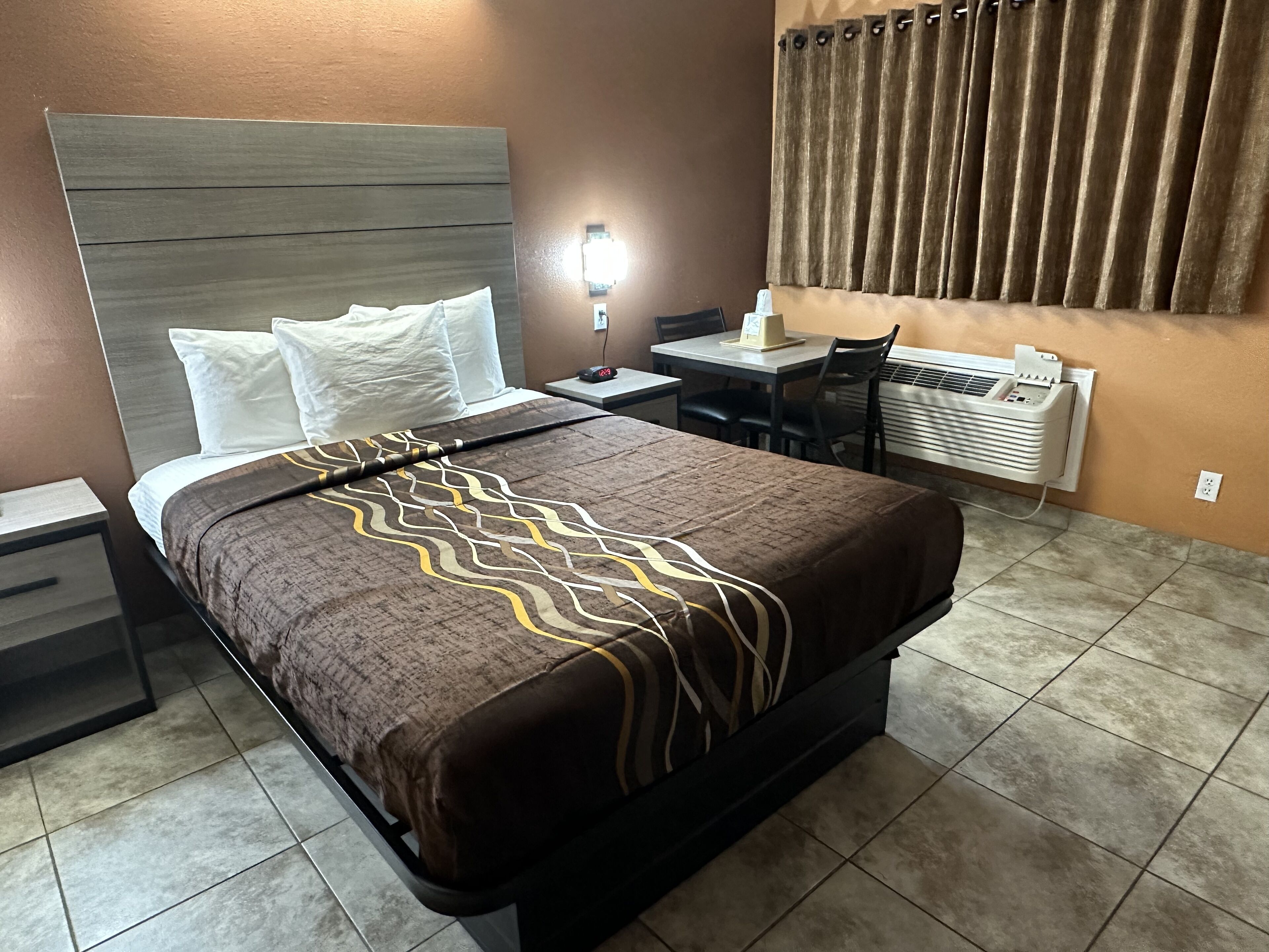 Habitación de hotel con cama, mesita de noche, escritorio, silla y equipo de aire acondicionado.
