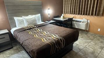 Habitación de hotel con cama, mesita de noche, escritorio, silla y equipo de aire acondicionado.