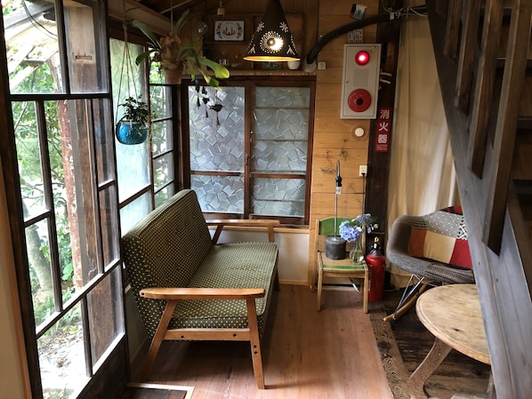 A cozy room with a wooden bench, a small table, and a sofa. There are windows with a view of greenery outside. - Ise Guesthouse Tsumugiya - Hostel (Ise)