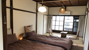 A traditional Japanese-style room with tatami flooring, a low wooden bed with two pillows, a small table, and a chair. - Ise Guesthouse Tsumugiya - Hostel (Ise)
