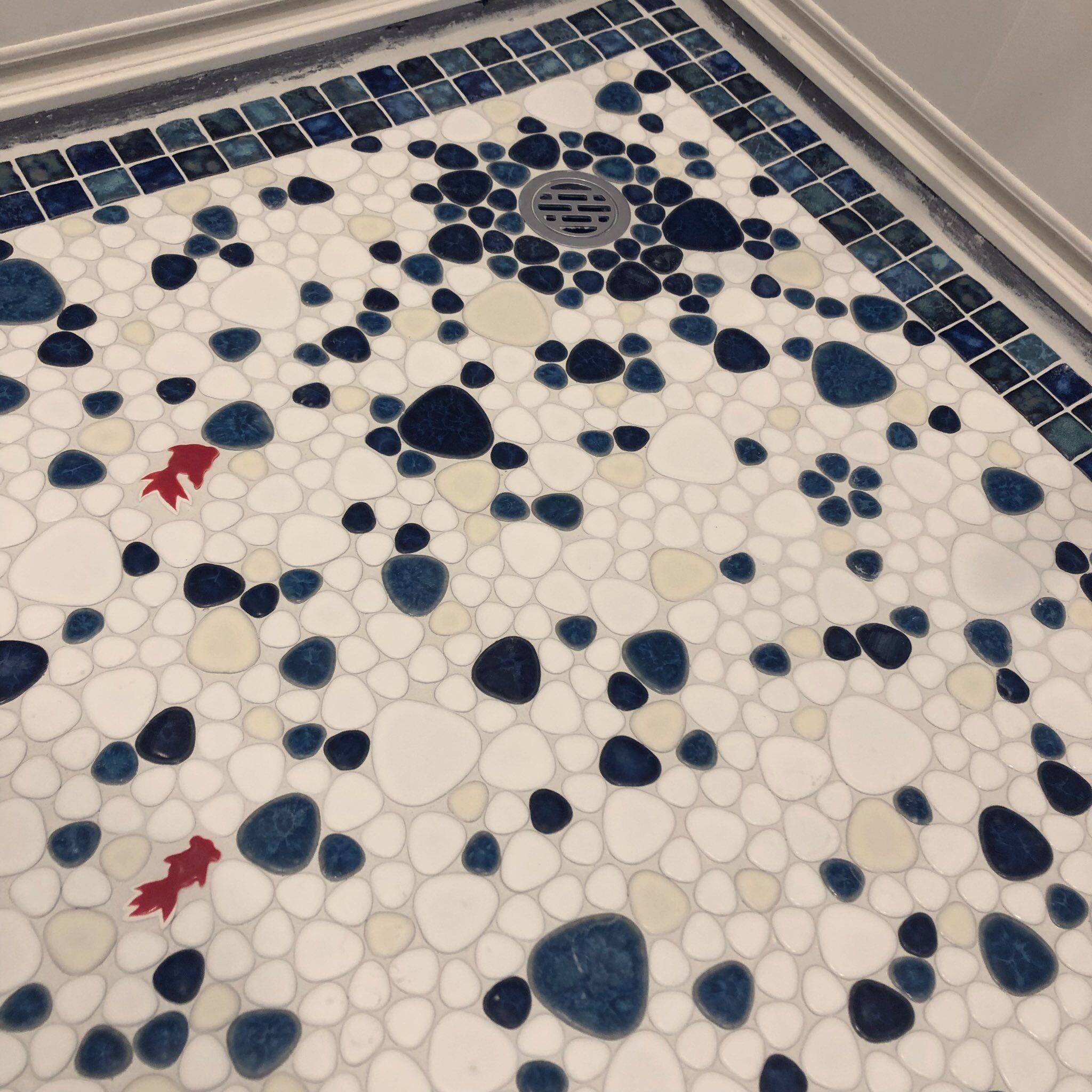 A bathroom floor with a mosaic tile pattern featuring large and small pebbles in white, blue, and red.
