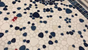 A bathroom floor with a mosaic tile pattern featuring large and small pebbles in white, blue, and red.