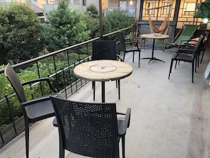 A balcony with outdoor seating, including chairs and a round table, surrounded by greenery and a railing. - Ise Guesthouse Tsumugiya - Hostel (Ise)