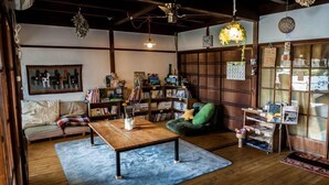 A cozy living room with a wooden coffee table, a sofa, and a bookshelf filled with books and decorative items. - Ise Guesthouse Tsumugiya - Hostel (Ise)