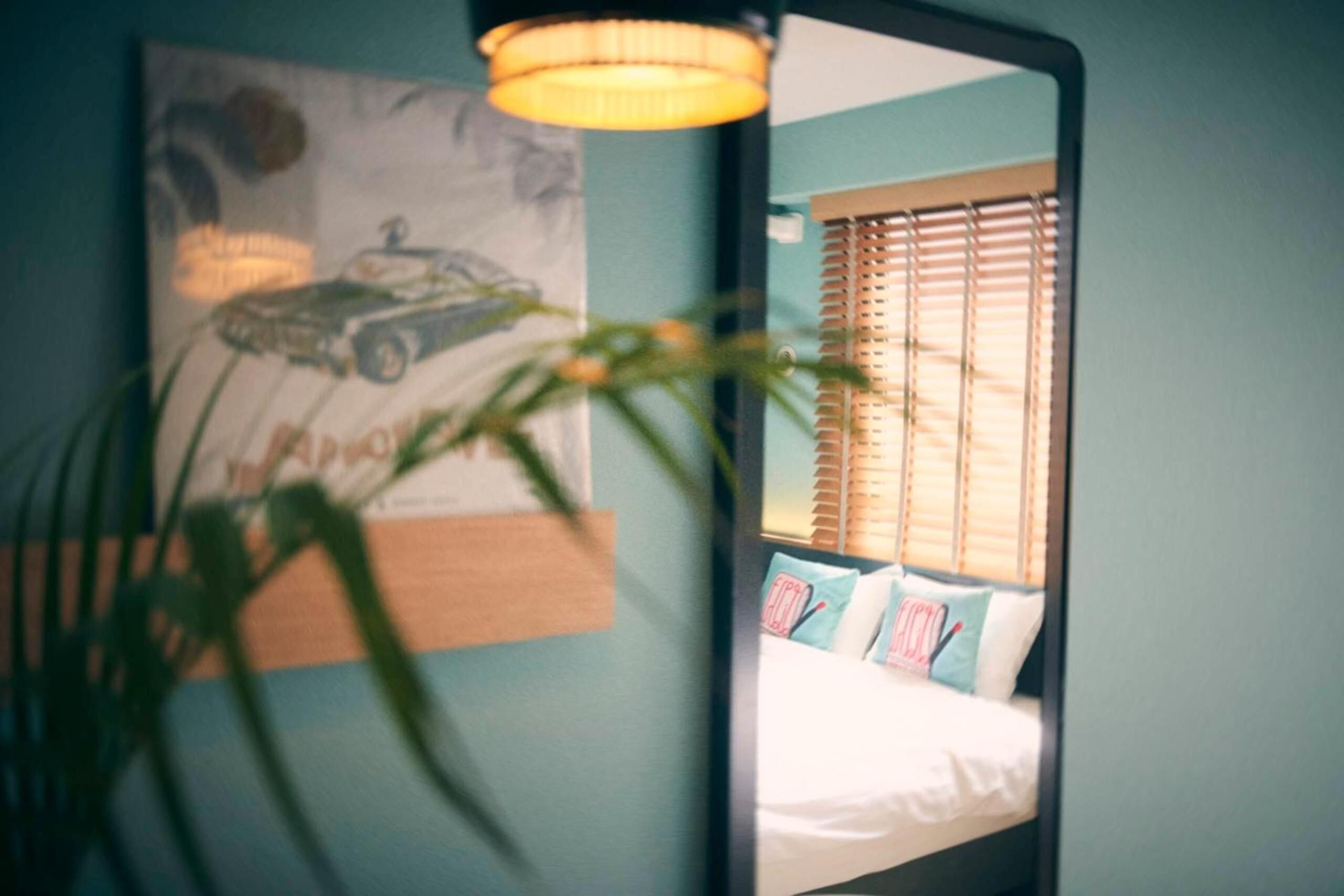 Une chambre à coucher avec un lit, une fenêtre avec des stores, un miroir fixé au mur et une affiche.